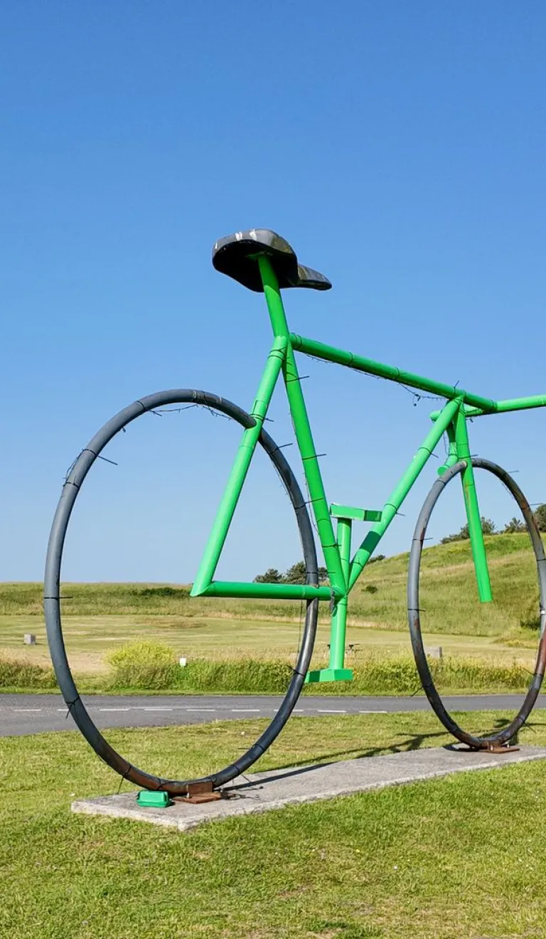 Green oversized bicycle sculpture standing beside parkland road in Pembrey Country Park.