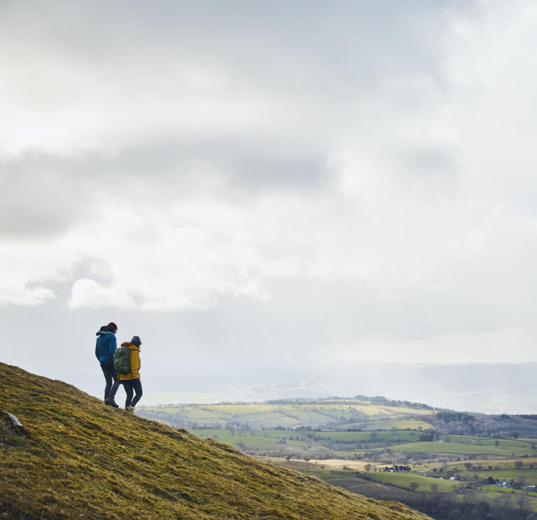 Two walkers on Hay Bluff looking out over countryside.