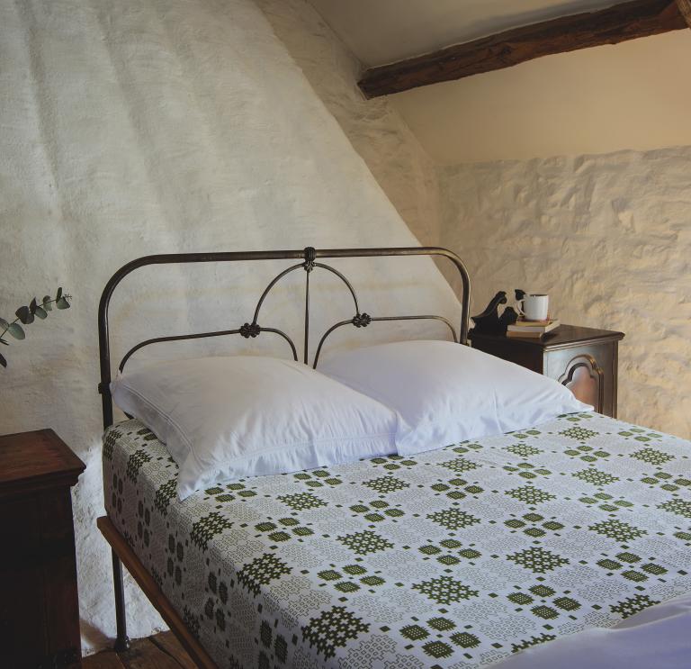 Traditional Welsh black iron bed with patterned green and white Welsh tapestry bed sheet.