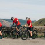 Four cyclists on road bikes by a stone wall overlooking mountains.